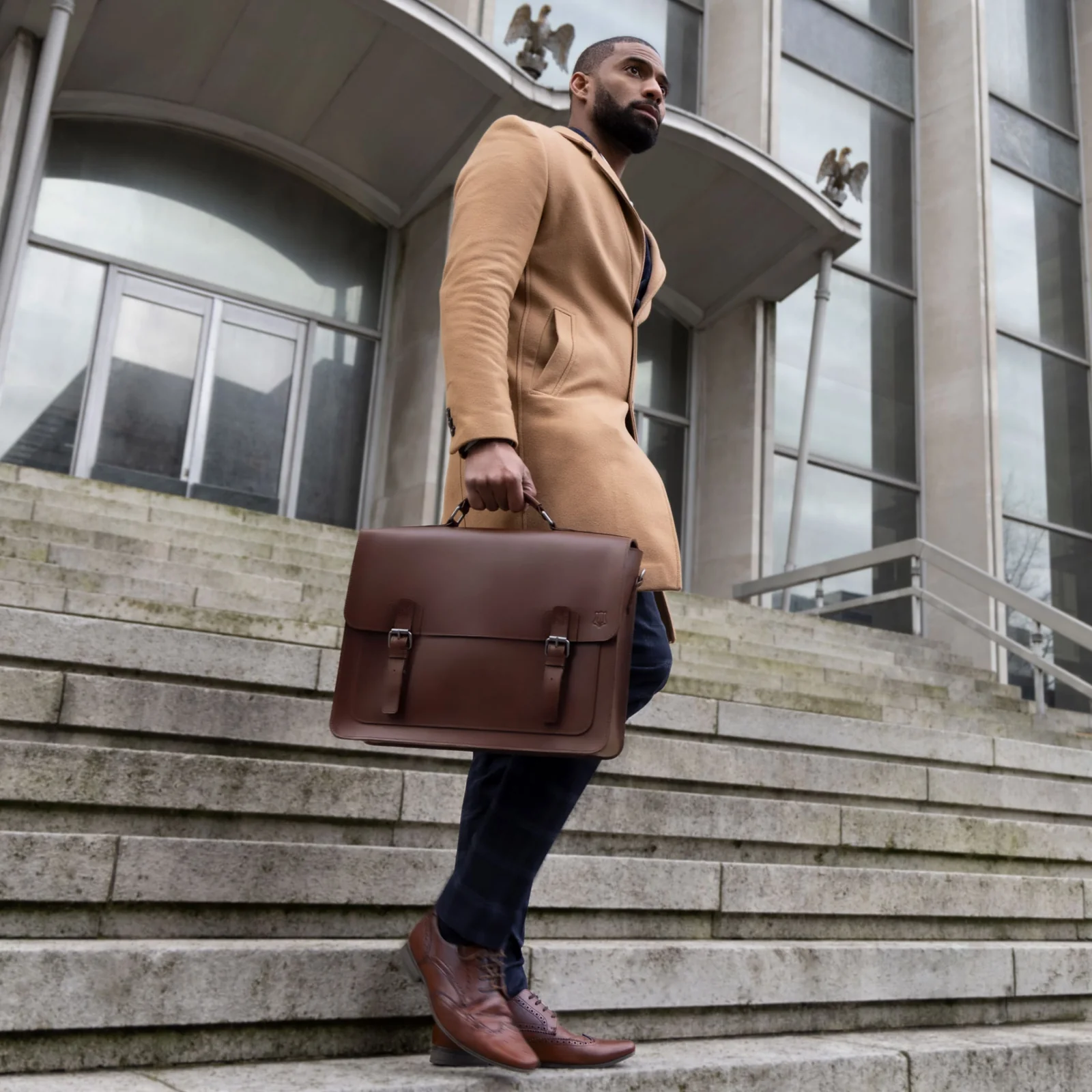 The Heritage carried by hand down city steps in a camel coat